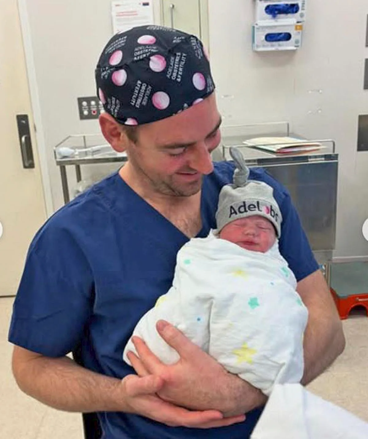 Callum is wearing hospital clothing while holding his newborn baby Fleur