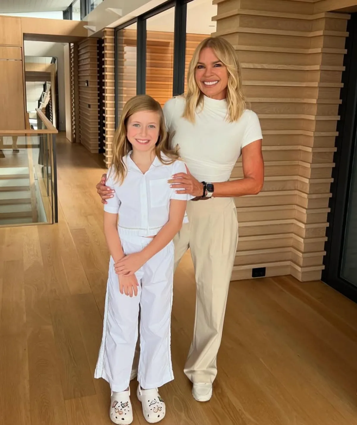 Sonia and her daughter pictured in the foyer of a beautiful home. Sonia wears a white short sleeved turtle neck and cream pants with her hair outand her daughter is in a white shirt and pants.