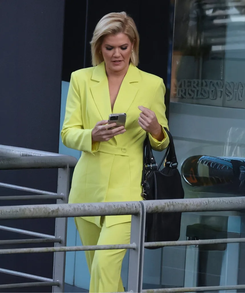 Sarah Harris is seen texting on her phone in a yellow suit