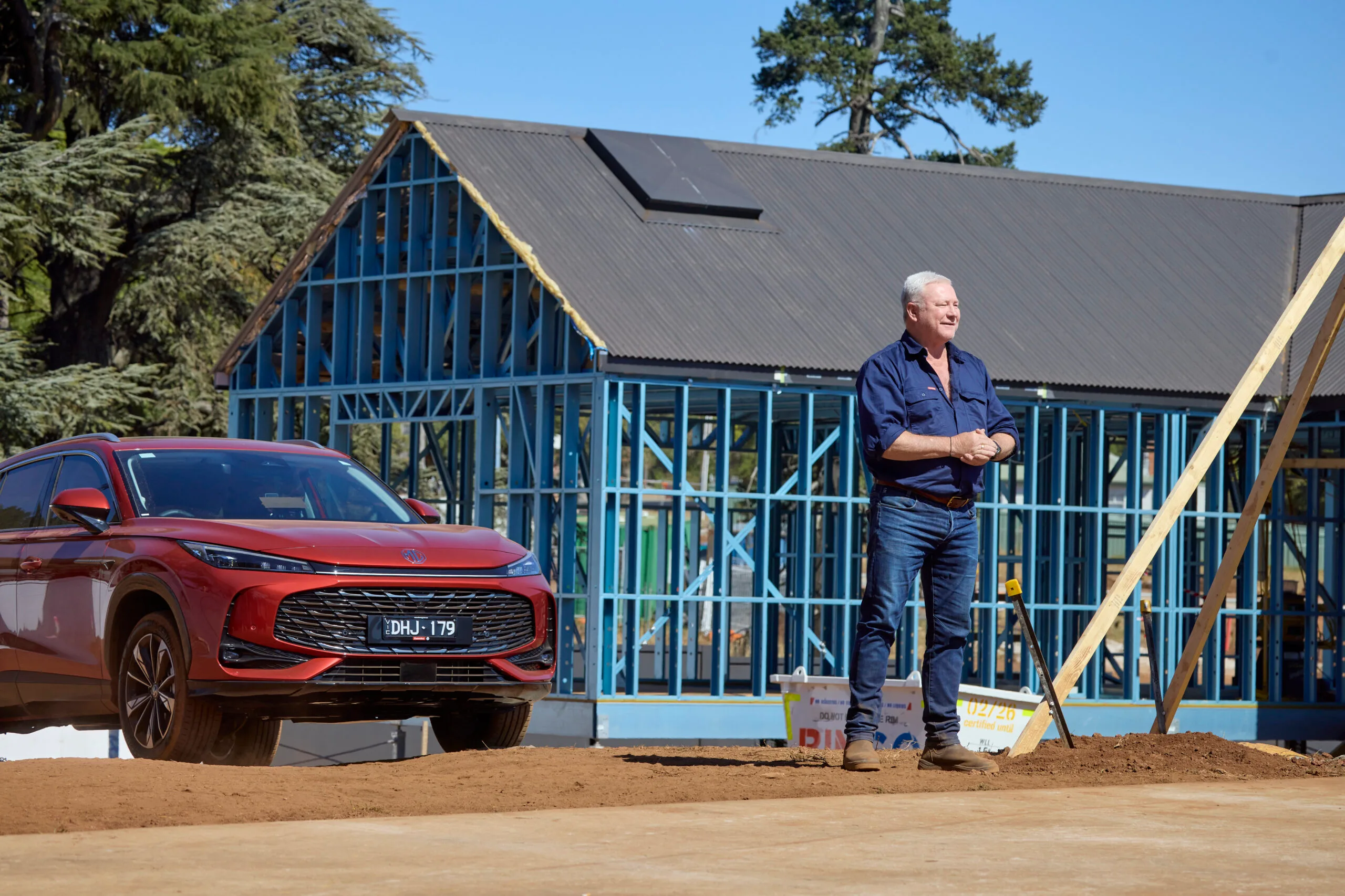 Scott Cam on site of The Block in front of one of the new builds in Daylesford. A red car is behind him as well.