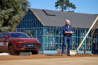 Scott Cam on site of The Block in front of one of the new builds in Daylesford. A red car is behind him as well.