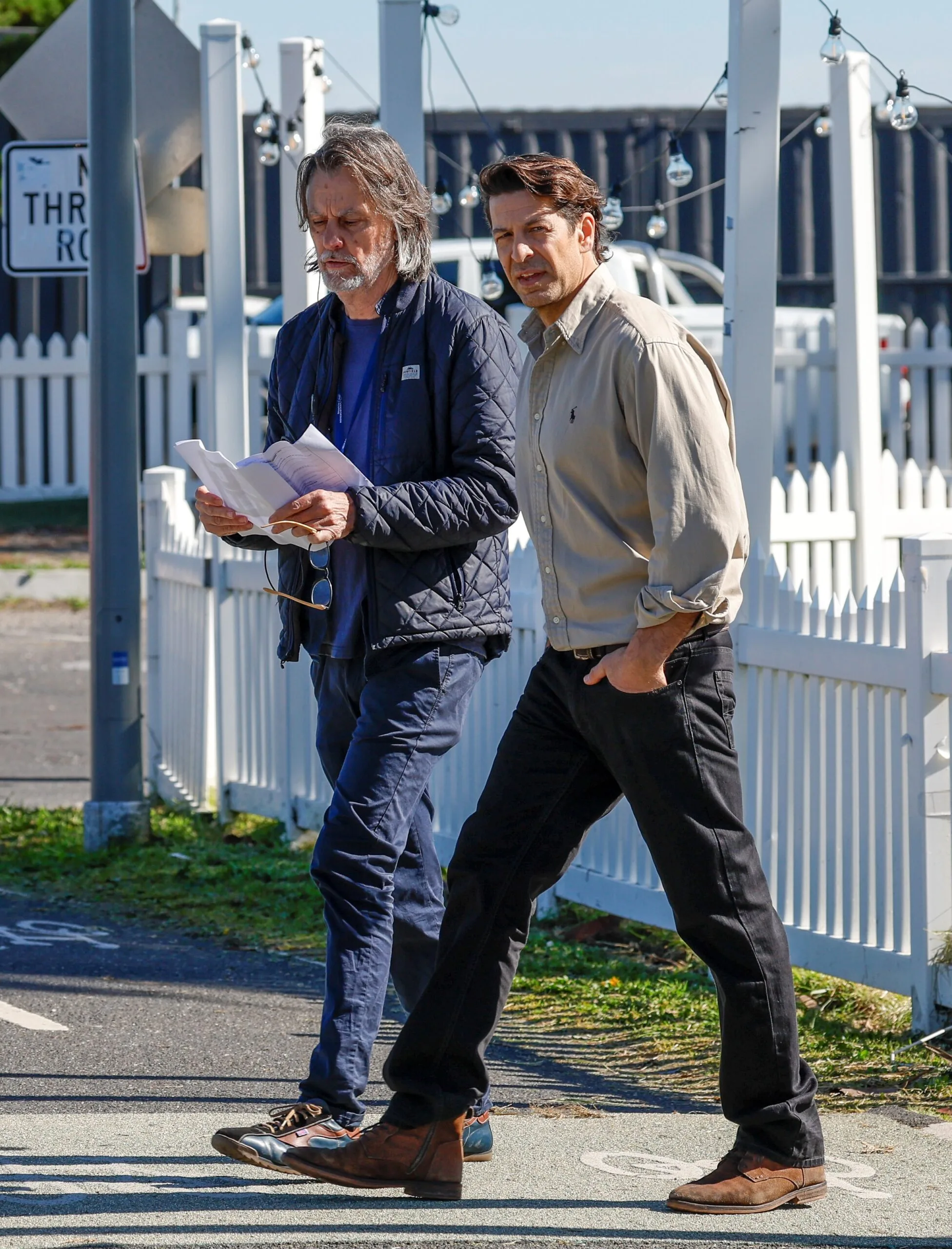 Don Hany walks past a white picket fence on the set of Imposter