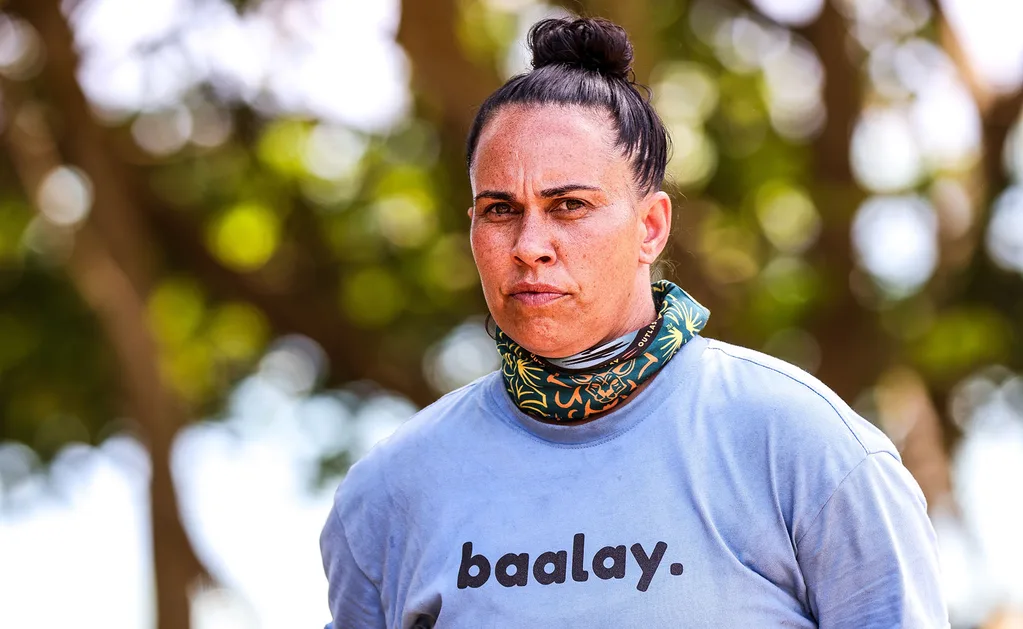 Kirby, wearing a blue t-shirt, with a buff around her neck, looks serious.