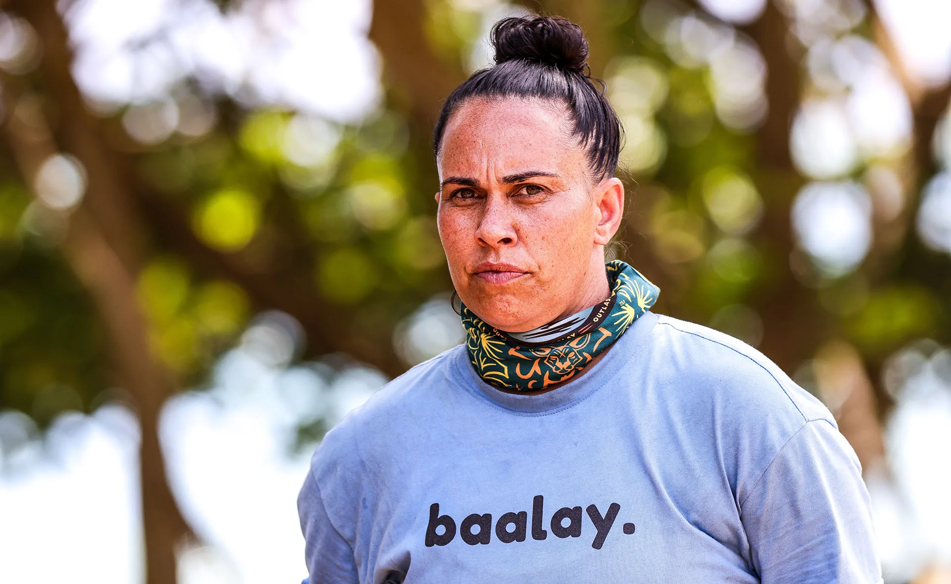 Kirby, wearing a blue t-shirt, with a buff around her neck, looks serious.