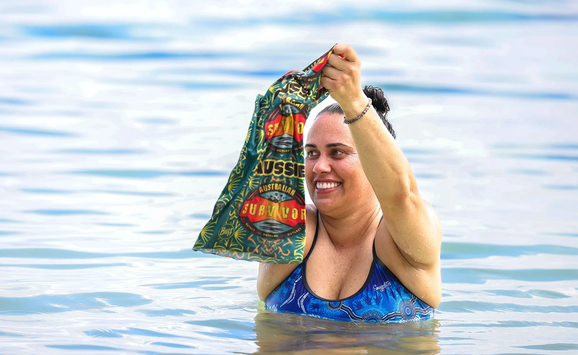 Kirby, wearing a swimsuit, holds up a Survivor buff while in the ocean.