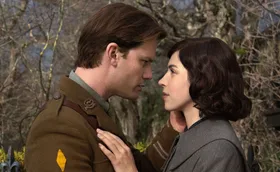 Jeremy Irvine, dressed in an army uniform, and Hermione Corfield, stare into each other's eyes on the set of Outlander: Blood Of My Blood