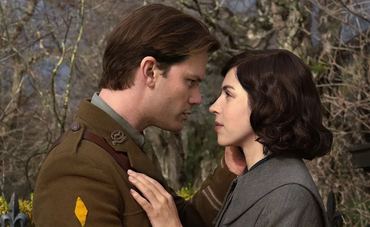 Jeremy Irvine, dressed in an army uniform, and Hermione Corfield, stare into each other's eyes on the set of Outlander: Blood Of My Blood