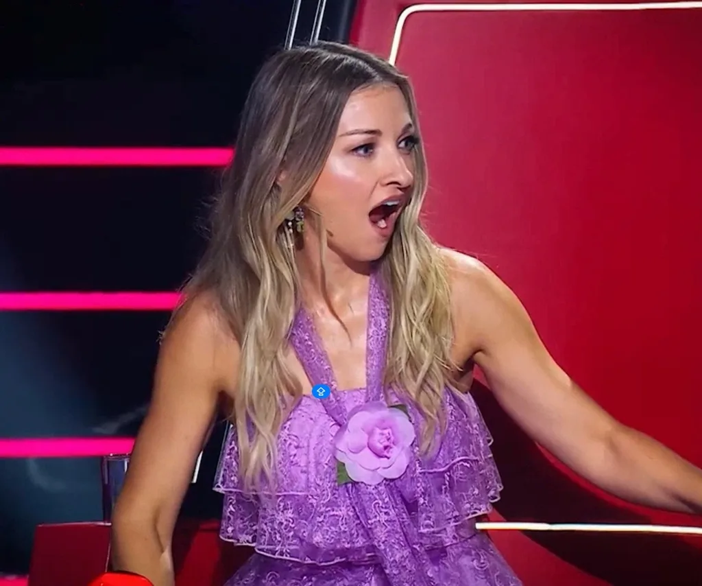 Kate Miller-Heidke sits on a red spinning chair in a purple dress looking shocked