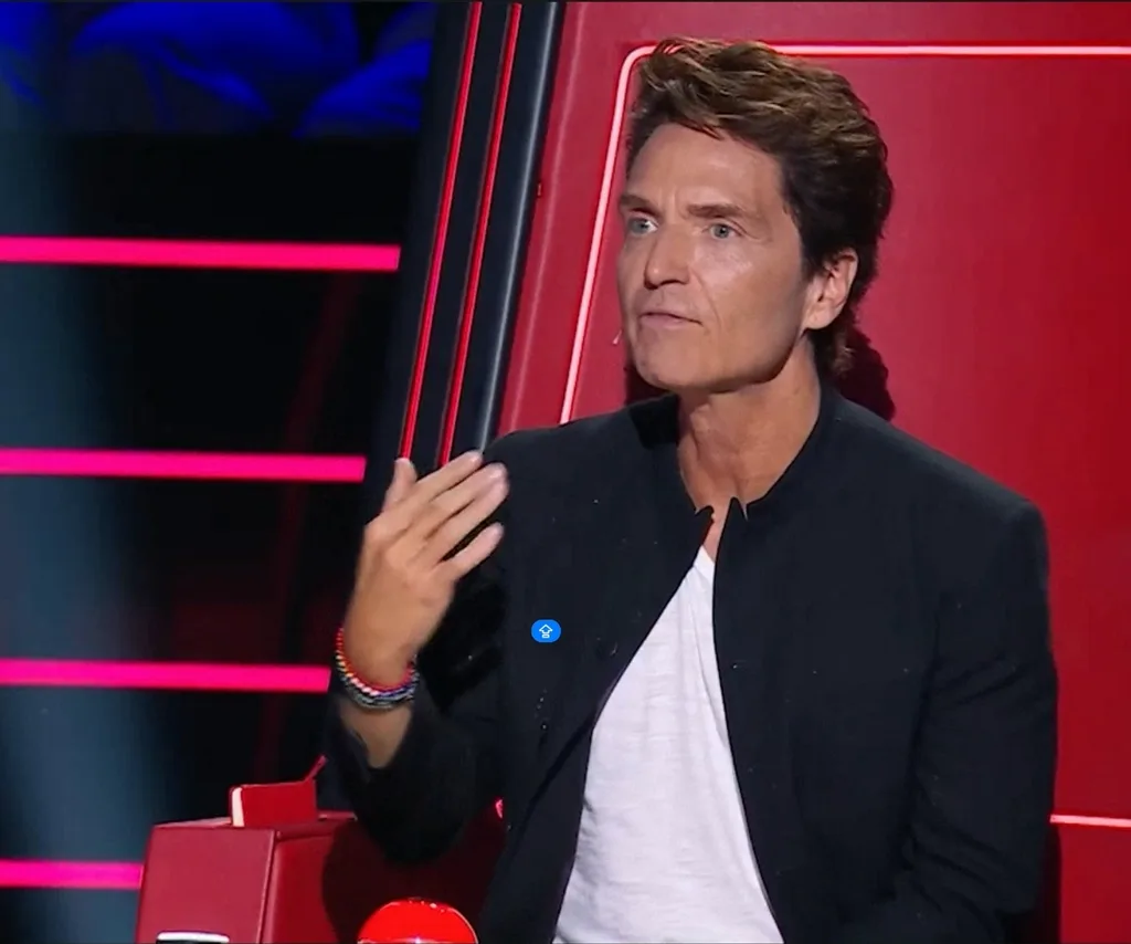 Richard sits on The Voice's red spinning chair in a white shirt and black blazer