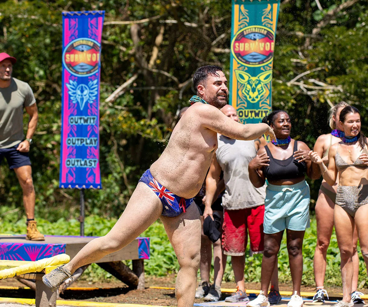 George, wearing budgie smugglers, throws something as part of a challenge on Survivor. 