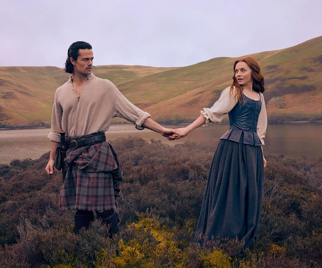 Jamie and Harriet hold hands, against a backdrop of the Scottish highlands, on the set of Blood Of My Blood.