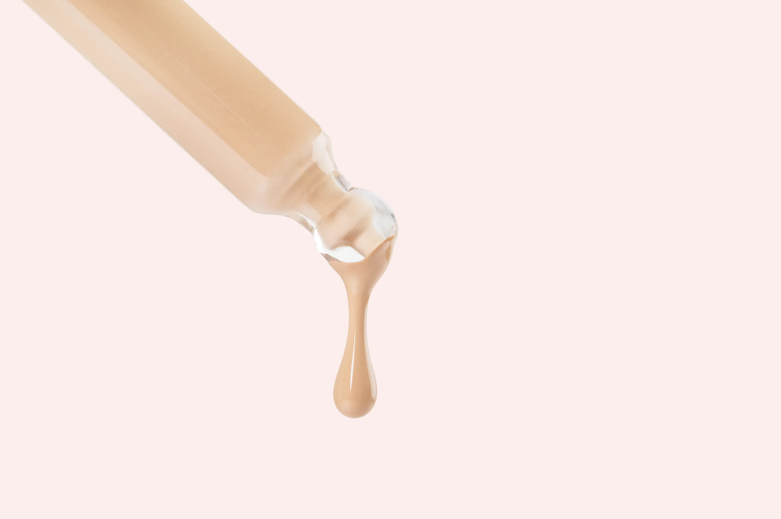 Foundation makeup dripping from a pipette on pink background