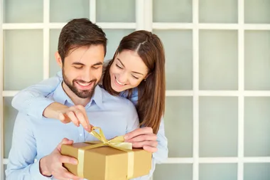Woman hugging a guy while he unwraps a golden gift