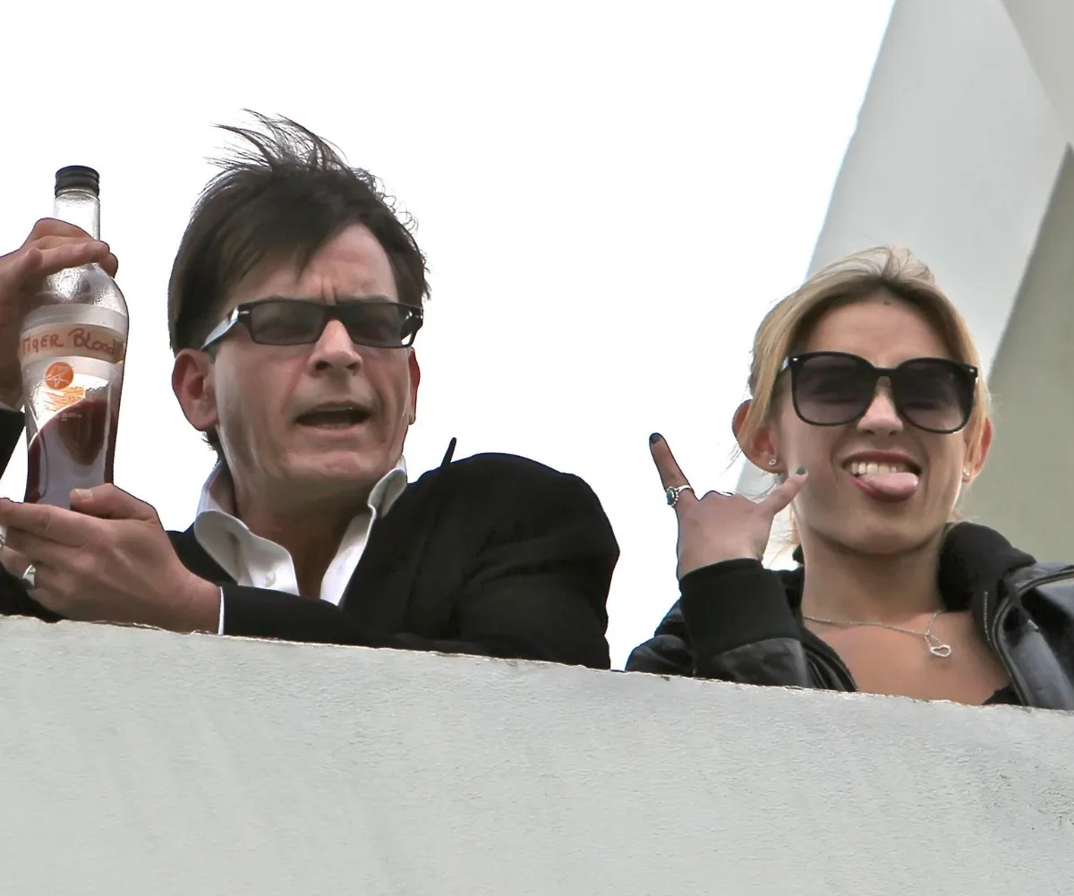 A man and women looking down from a balcony. The man is holding a bottle of alcohol.