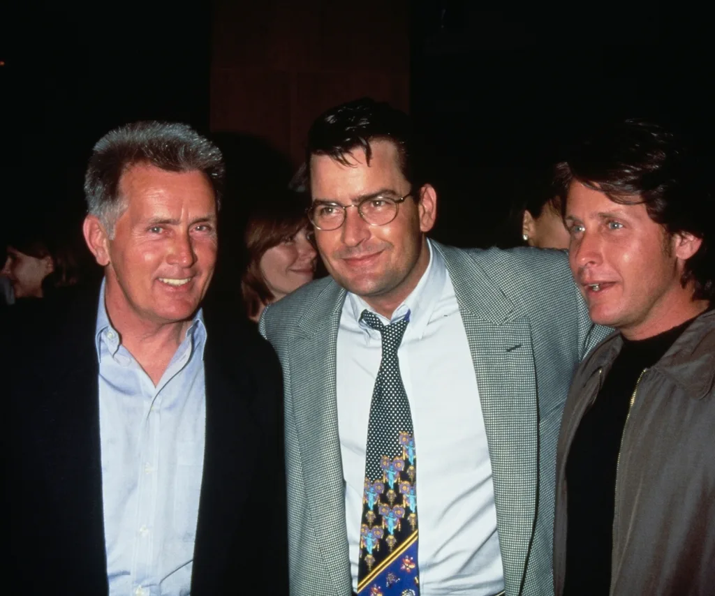 Three men with the middle one's arms around the others