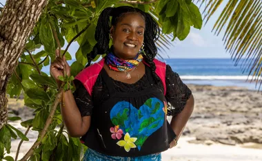 Cirie stands, with her hands on her hips, on a beach in Samoa.