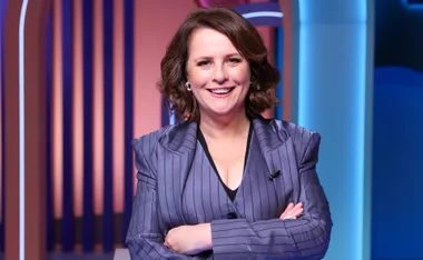 Anne Edmonds, wearing a purple jacket, stands with her arms folded on the set of Talkin' 'Bout Your Gen.