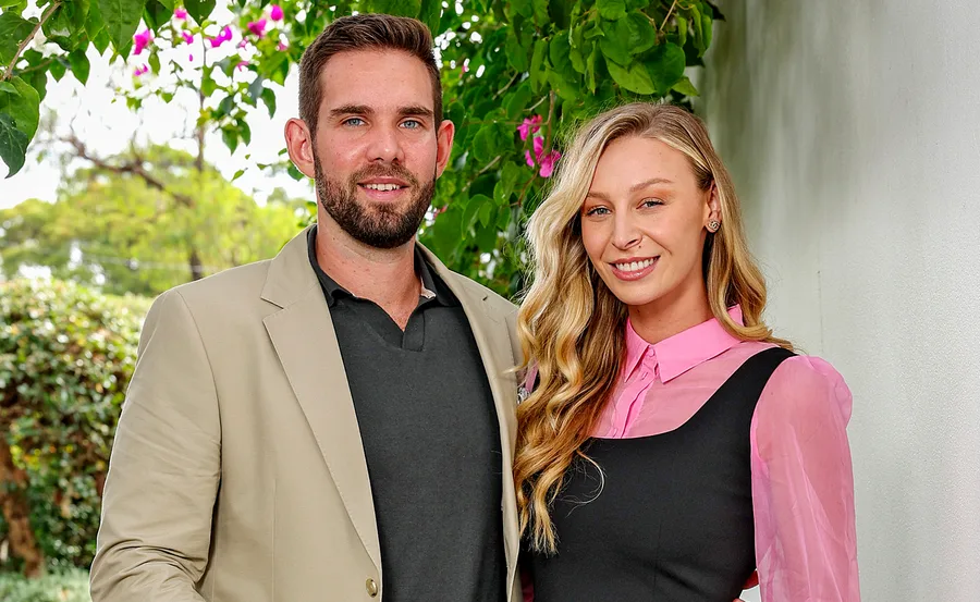Michael, in a black shirt and beige jacket, and Rielli, in a pink and black outfit, stand together on the street outside a home