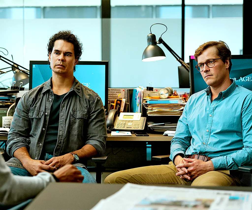 Mark, in character as Justin in Apple Cider Vinegar, sits at a desk in an office, with Richard Davies, as Sean, sitting next to him.