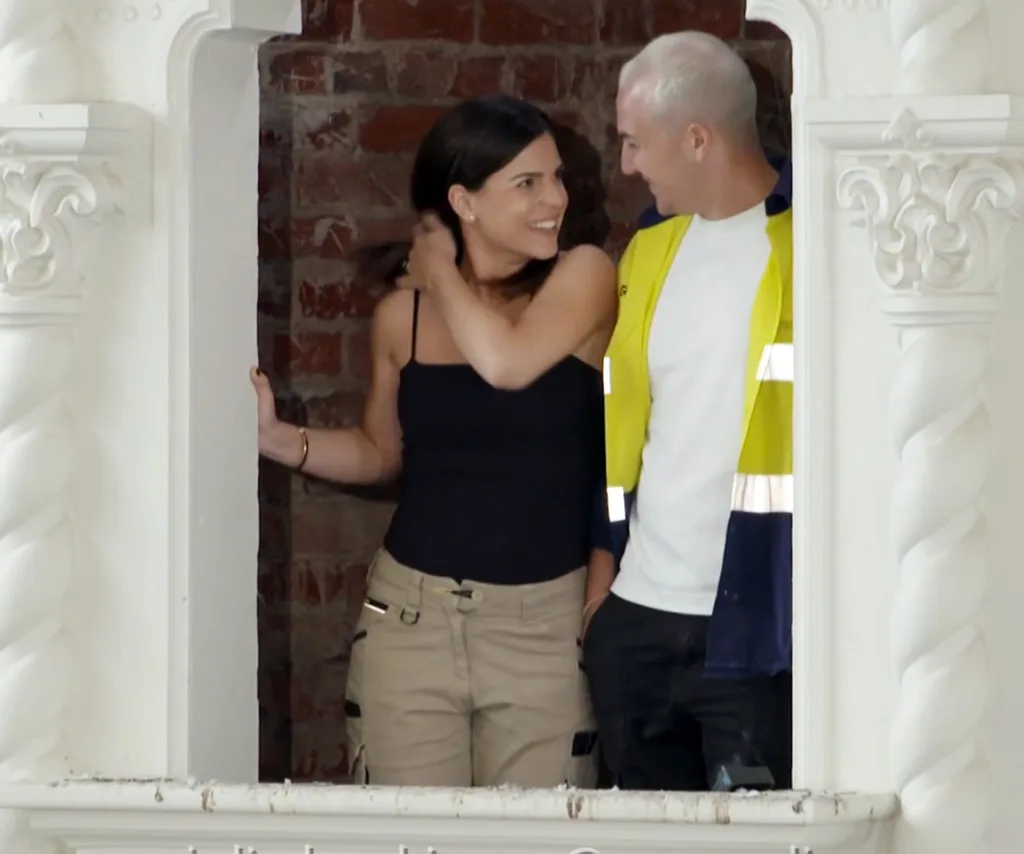 Steph and Gian stand in a window smiling at each other on set of a challenge for the 2025 series of The Block.