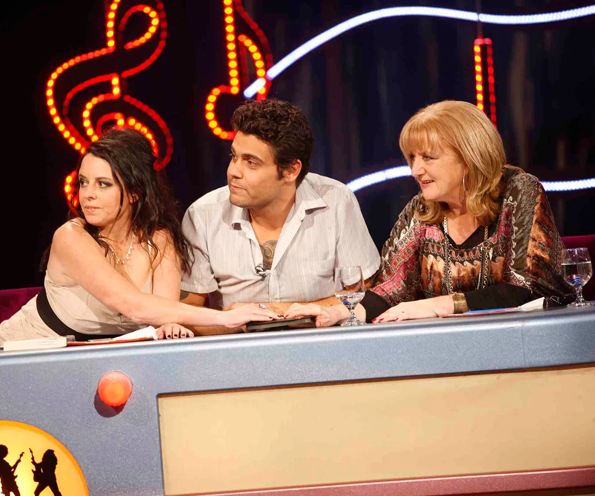 Denise sitting behind the desk, on Myf Warhurst's team, on the set of Spicks & Specks