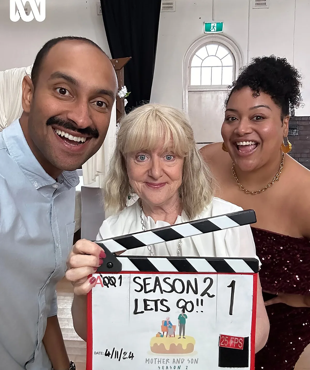 Denise, holding a clapperboard, stands in between her co-stars Matt Okine and Angela Nica Sullen 