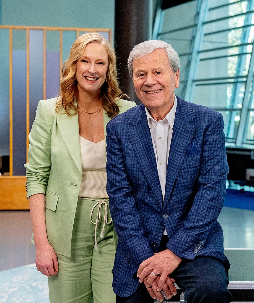 Leigh, in a green suit, stands next to Ray Martin, in a blue jacket, on the set of The Assembly