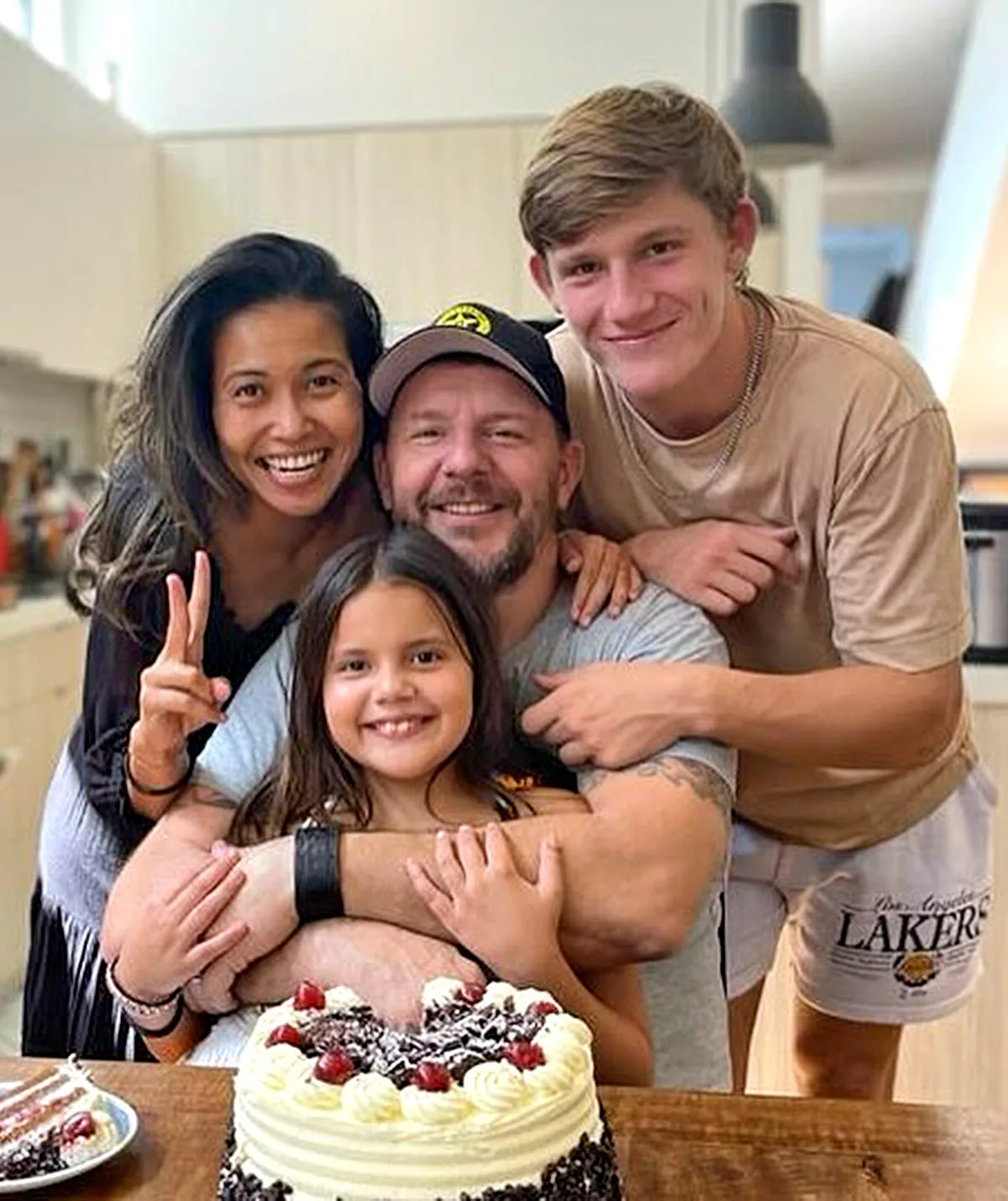 My Kitchen Rules judge Manu and his wife and kids pose for a photo in front of a cake.