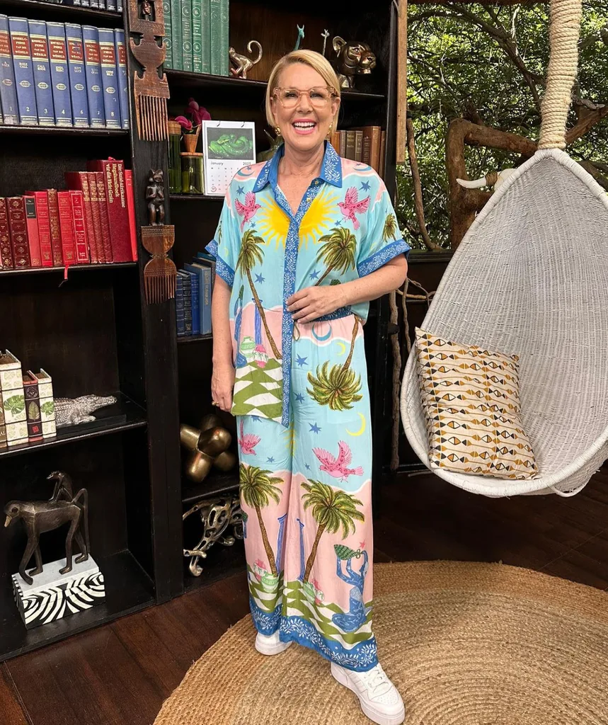 Woman in colourful dress standing in front of bookshelf and smiling at camera.