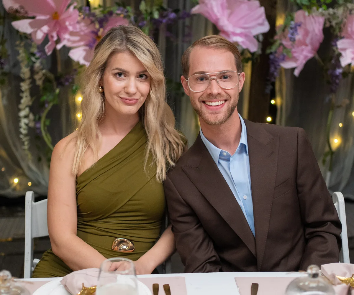 Maria, wearing an olive green dress, sits next to Mark, wearing a blue shirt and brown jacket, at a dinner table