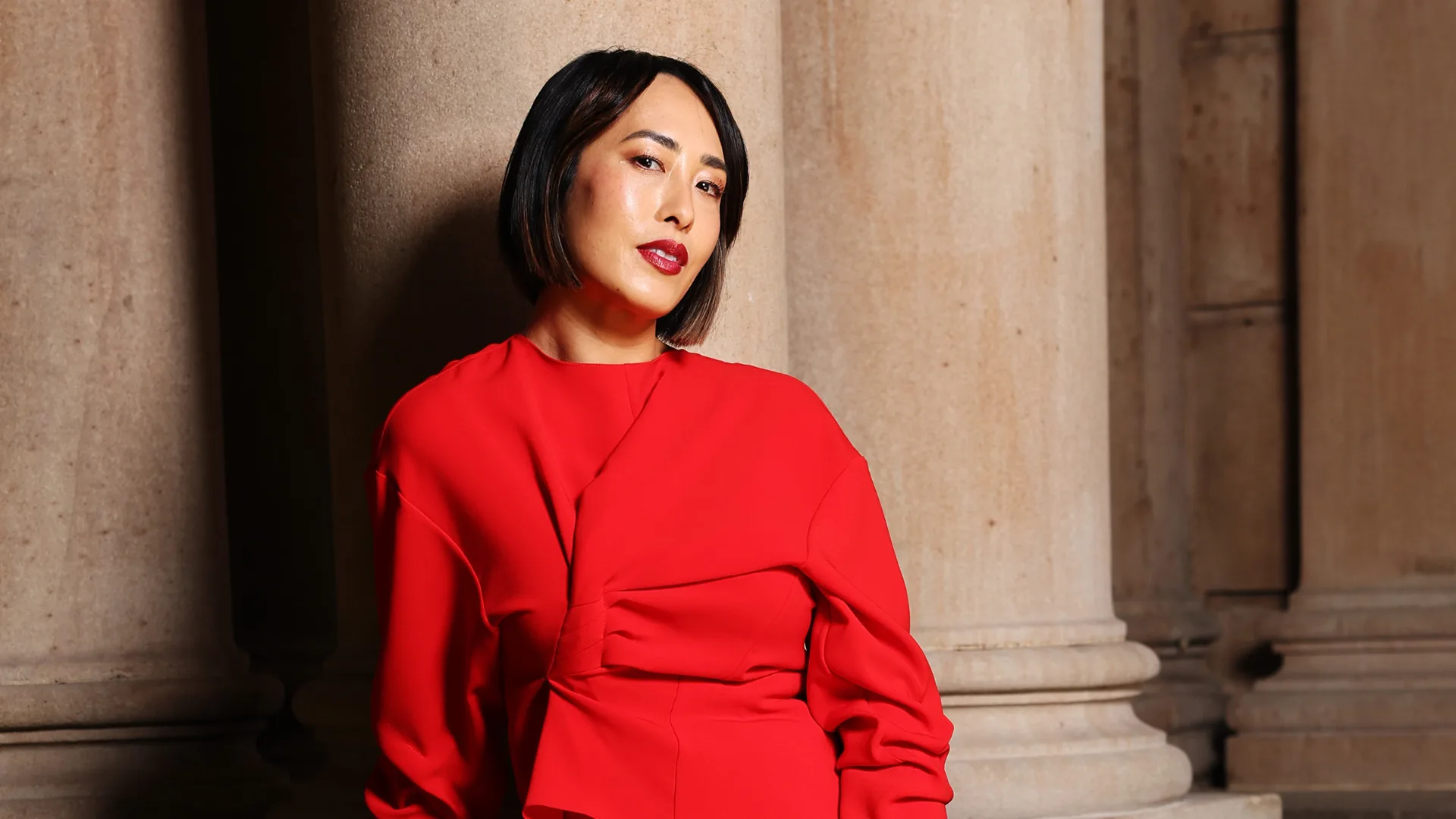 Woman in red dress poses against pillar