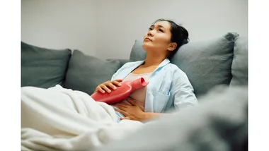 A woman in pain clutches a hot water bottle to her abdomen.
