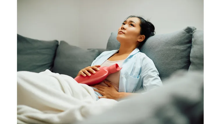 A woman in pain clutches a hot water bottle to her abdomen.