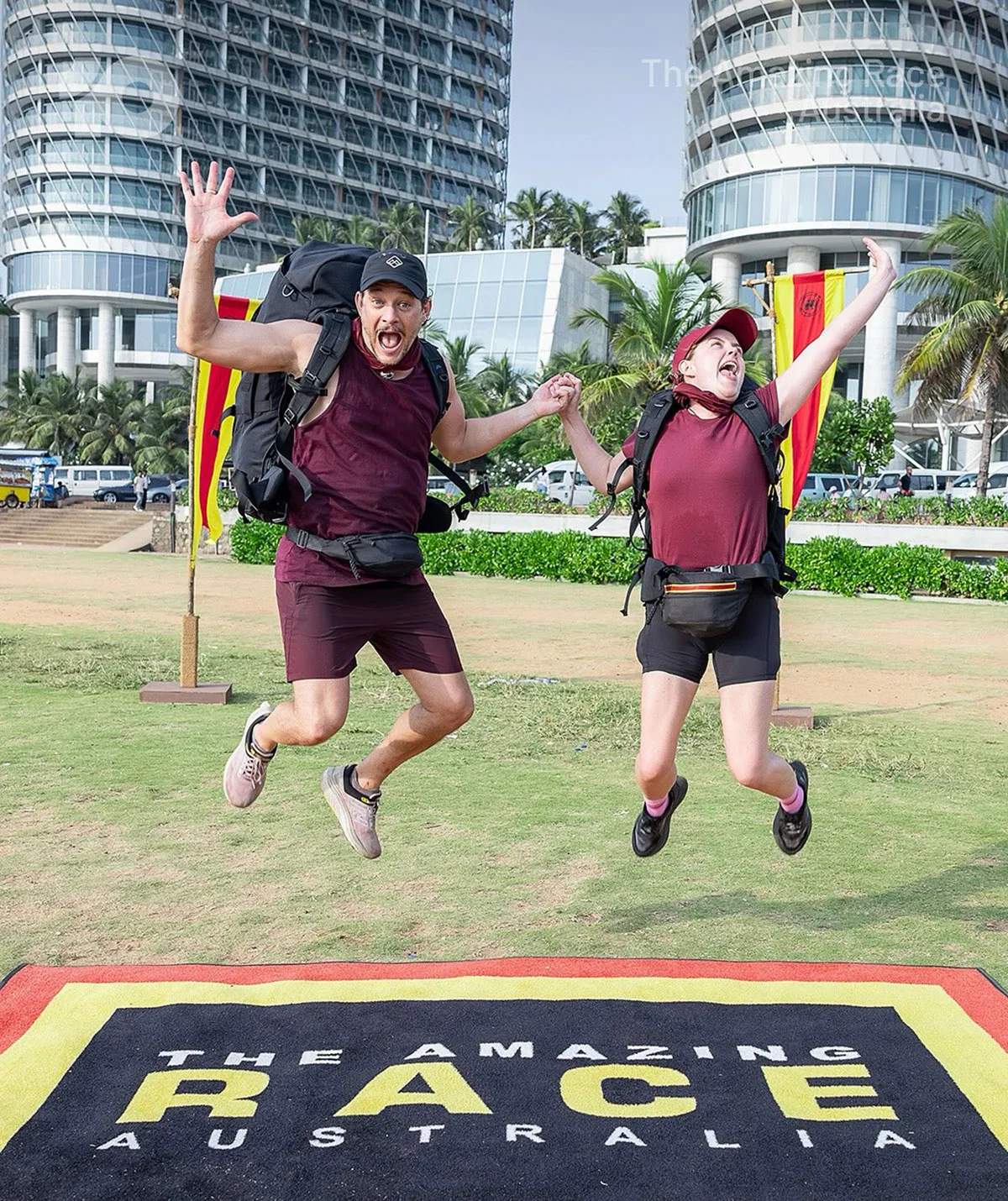 Rob Mills and Georgie Tunny jump for joy on The Amazing Race: Celebrity Edition 2025 pit stop sign.