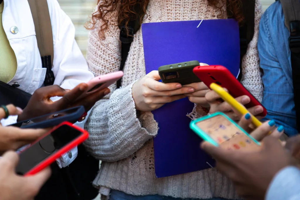 Close up of young college students hands holding mobile phones. Teenagers addicted to smartphones and technology. Group of friends sharing content on social media. Technology concept.