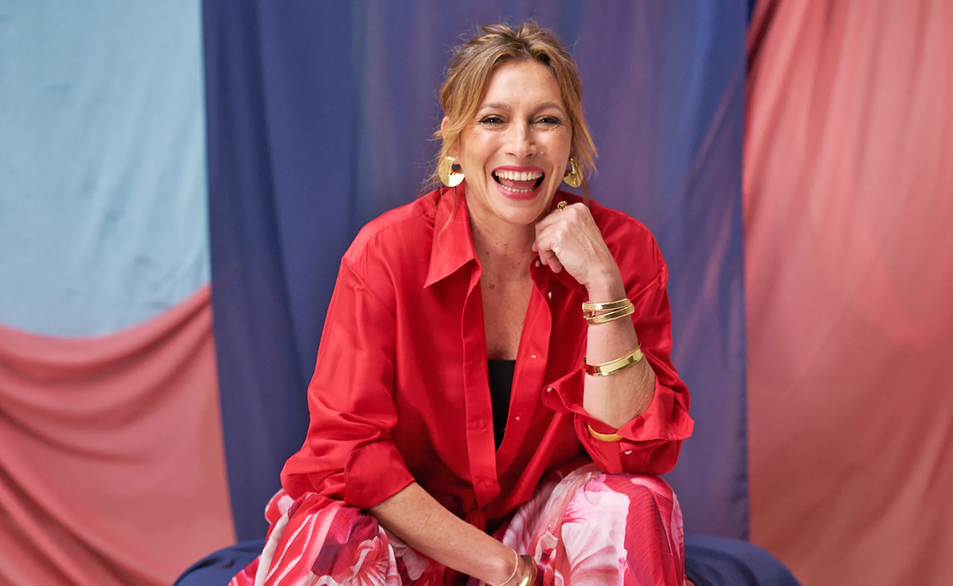 Claudia Karvan, in a red shirt, smiles at the camera