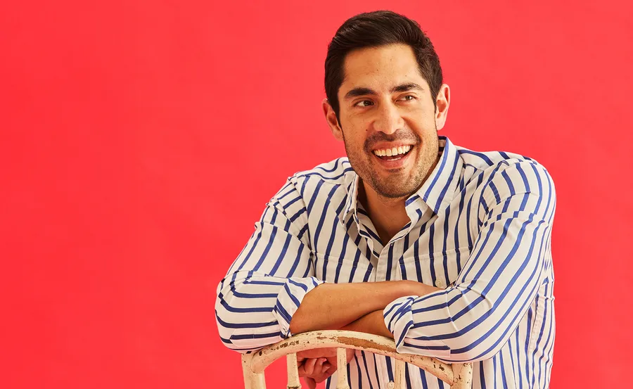 Tai Hara in a black and white stripe shirt against a red backdrop.
