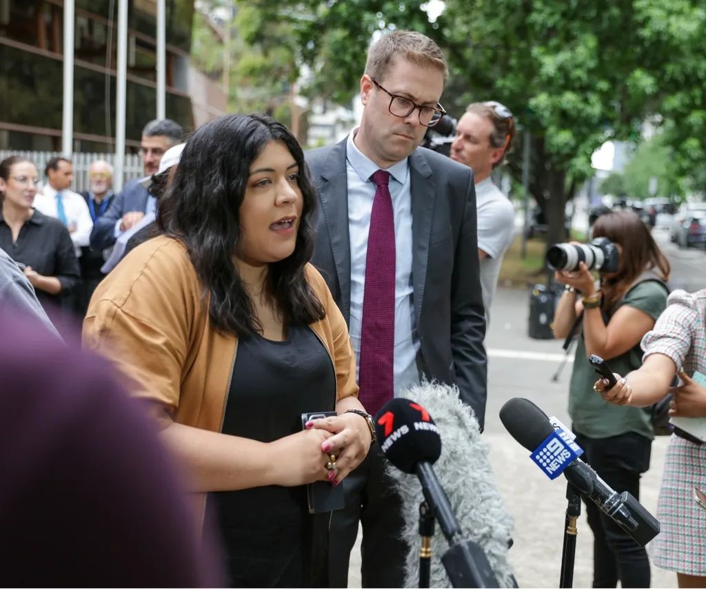 A woman speaks at a press conference surrounded by people.