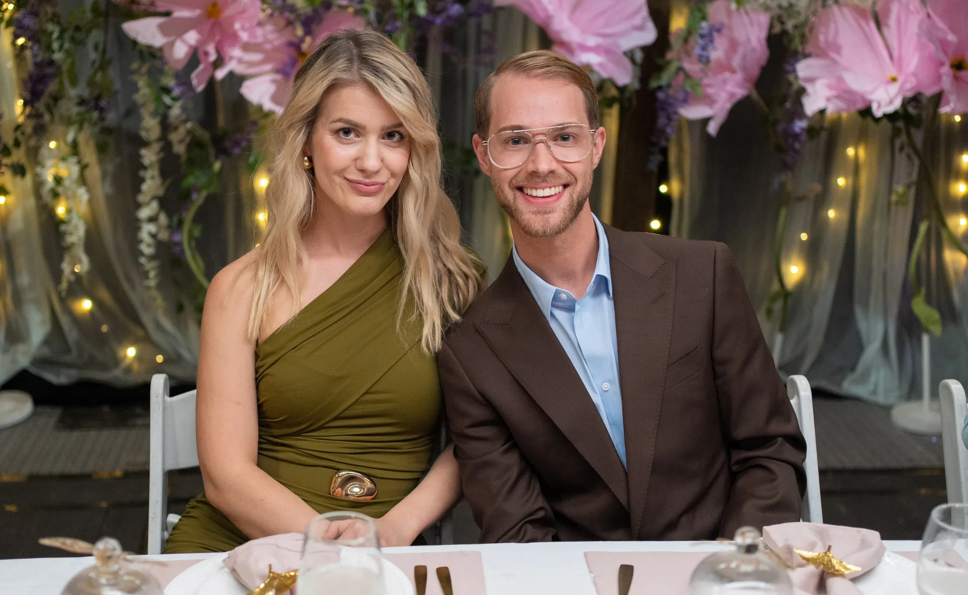 Maria, in an olive dress, sits next to Bailey, in a blue shirt and brown jacket, at an instant restaurant.