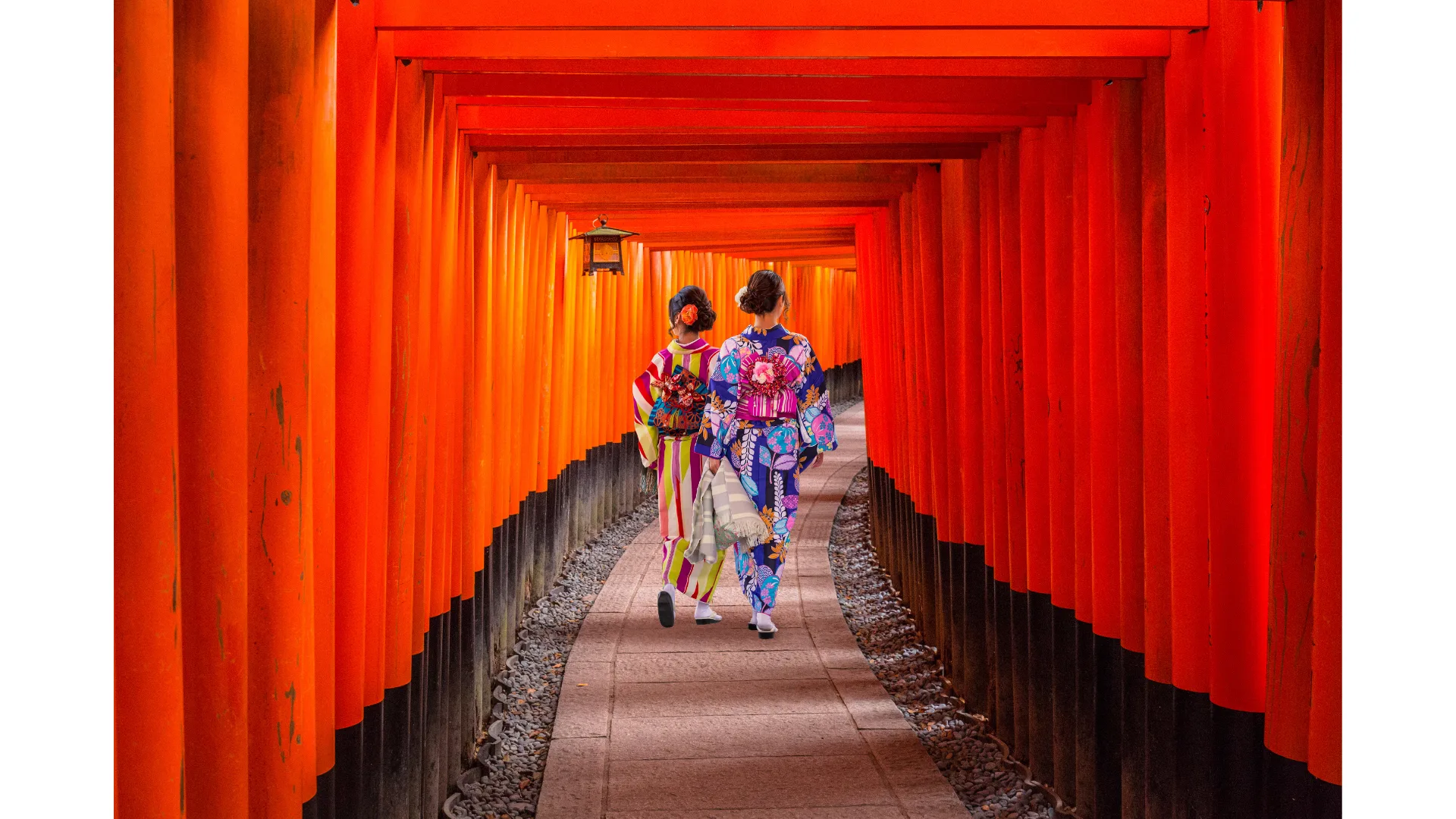 Two women in kimonos walk through the red gates of Fushimi Inari Taisha.