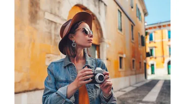 A woman holds a camera while exploring a European city.
