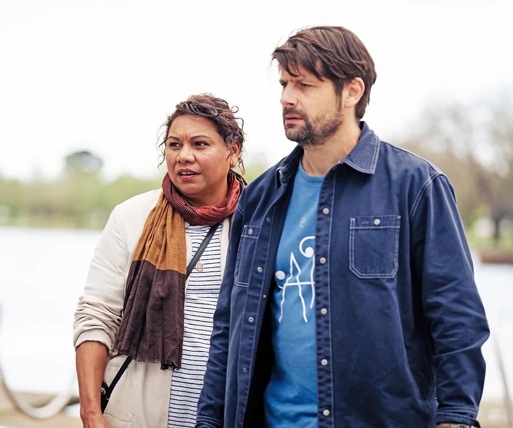 Deborah Mailman, wearing a scarf, stands next to Ryan Johnson, in a denim jacket, in character on Dear Life