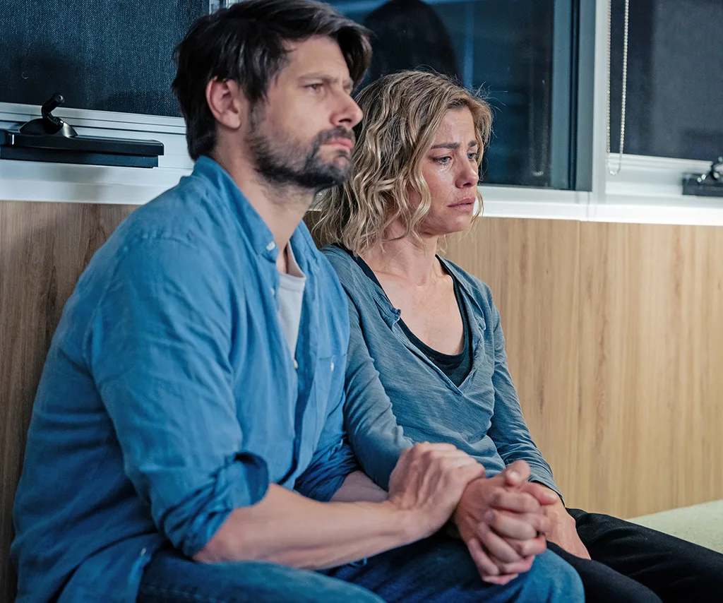 Brooke sits next to Ryan Johnson, holding hands with him and looking very sad, on the set of Dear Life