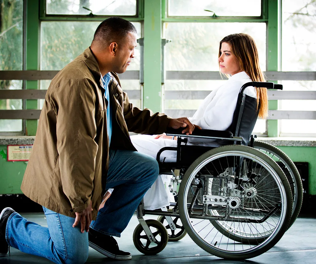 Brooke sits in a wheelchair with a window behind her on the set of Black Comedy