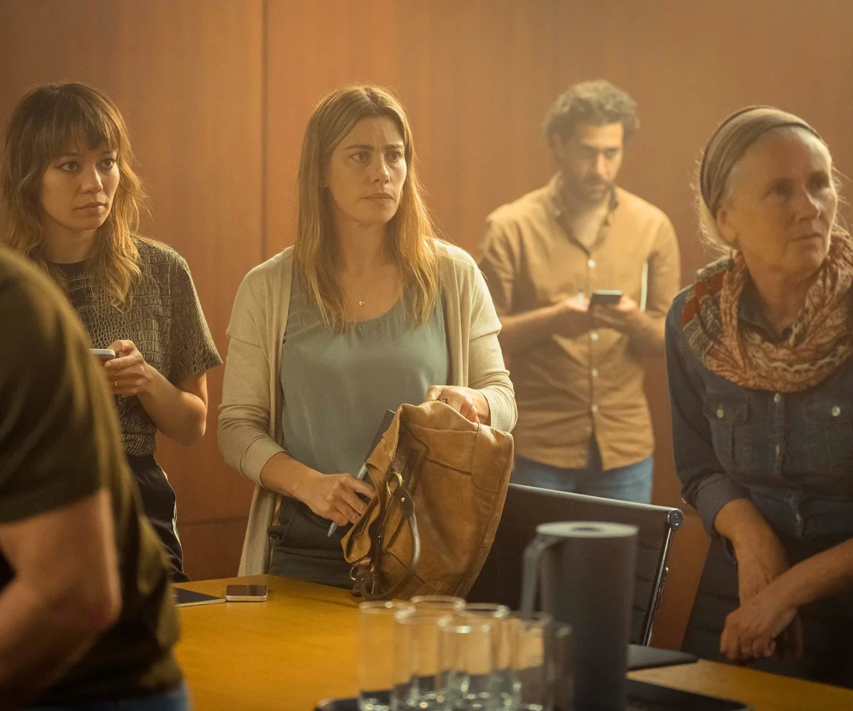 Brooke, playing a juror in The Twelve, stands in a room full of people