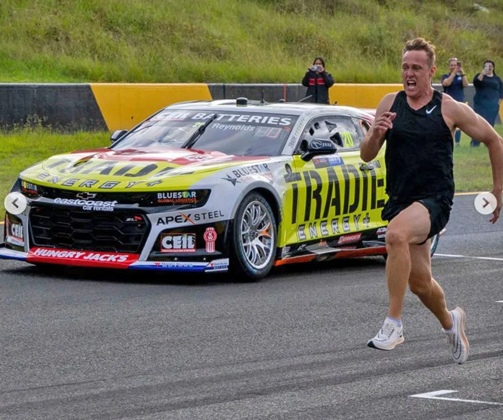Matt runs on a racetrack next to a V8 Supercar