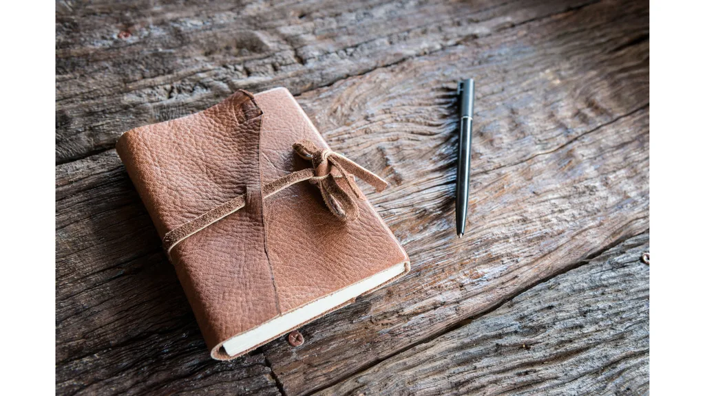 A leather bound journal and pen sit on a wooden table.
