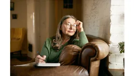 A woman sits on a coach while writing in her diary.