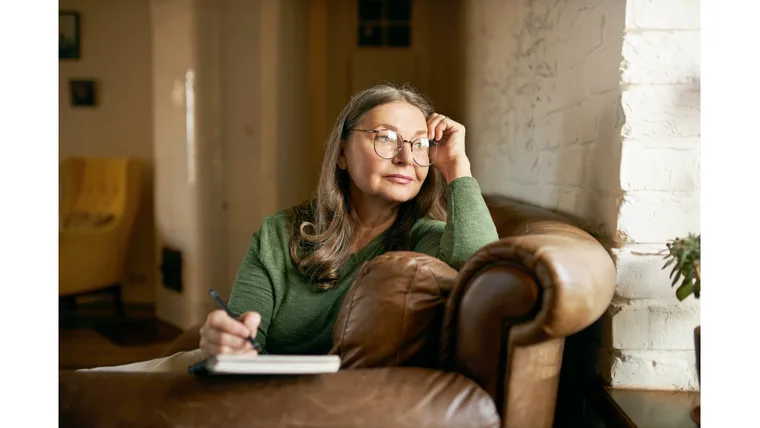 A woman sits on a coach while writing in her diary.