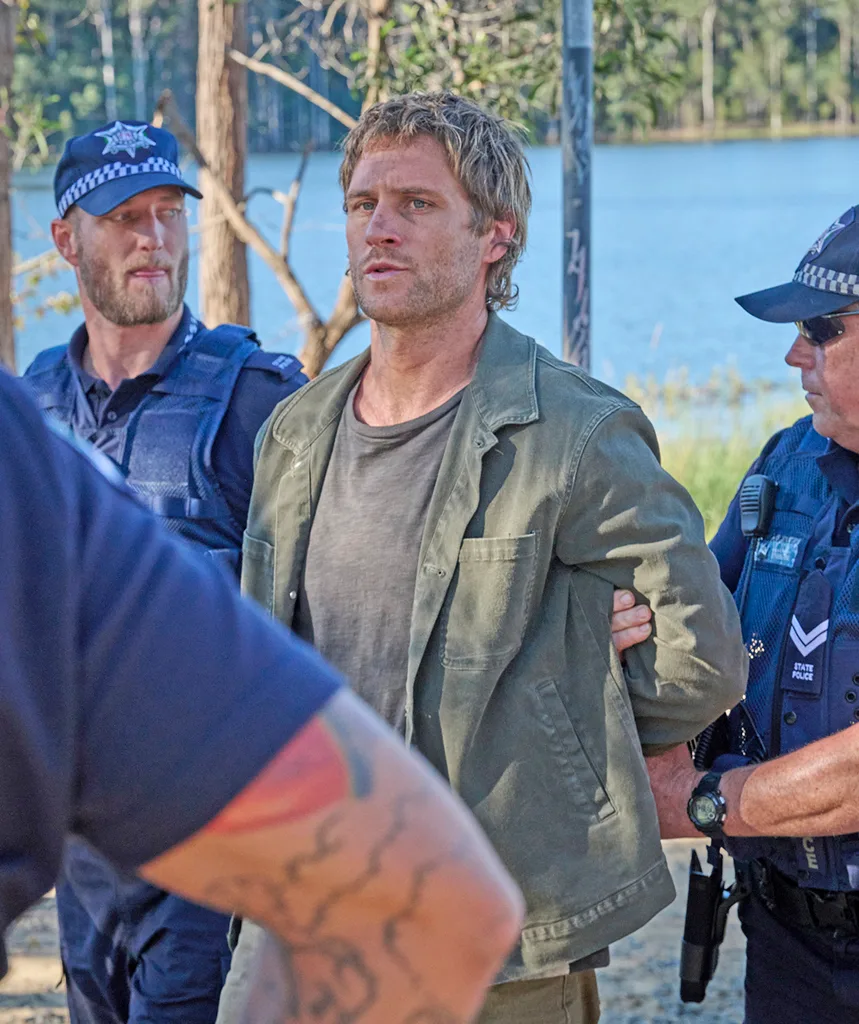 George, in character on the set of Black Snow, has his arms held behind his back by police officers